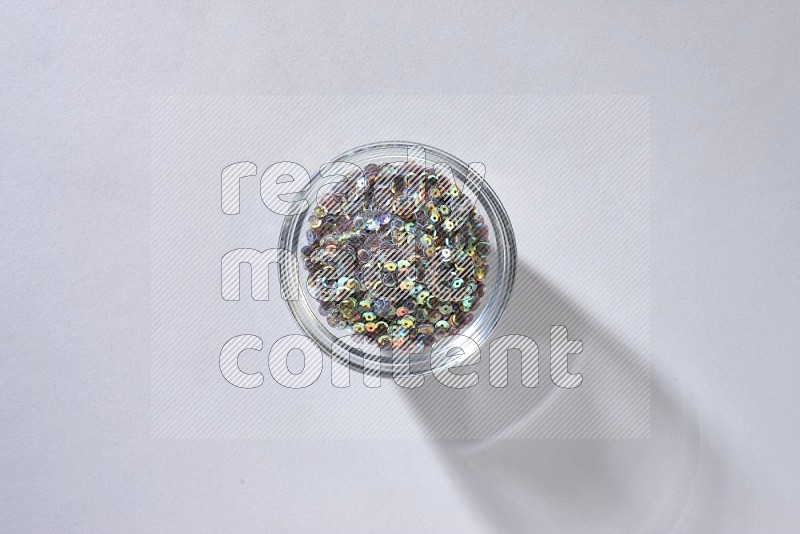 A glass bowl full of colored flat sequins on grey background