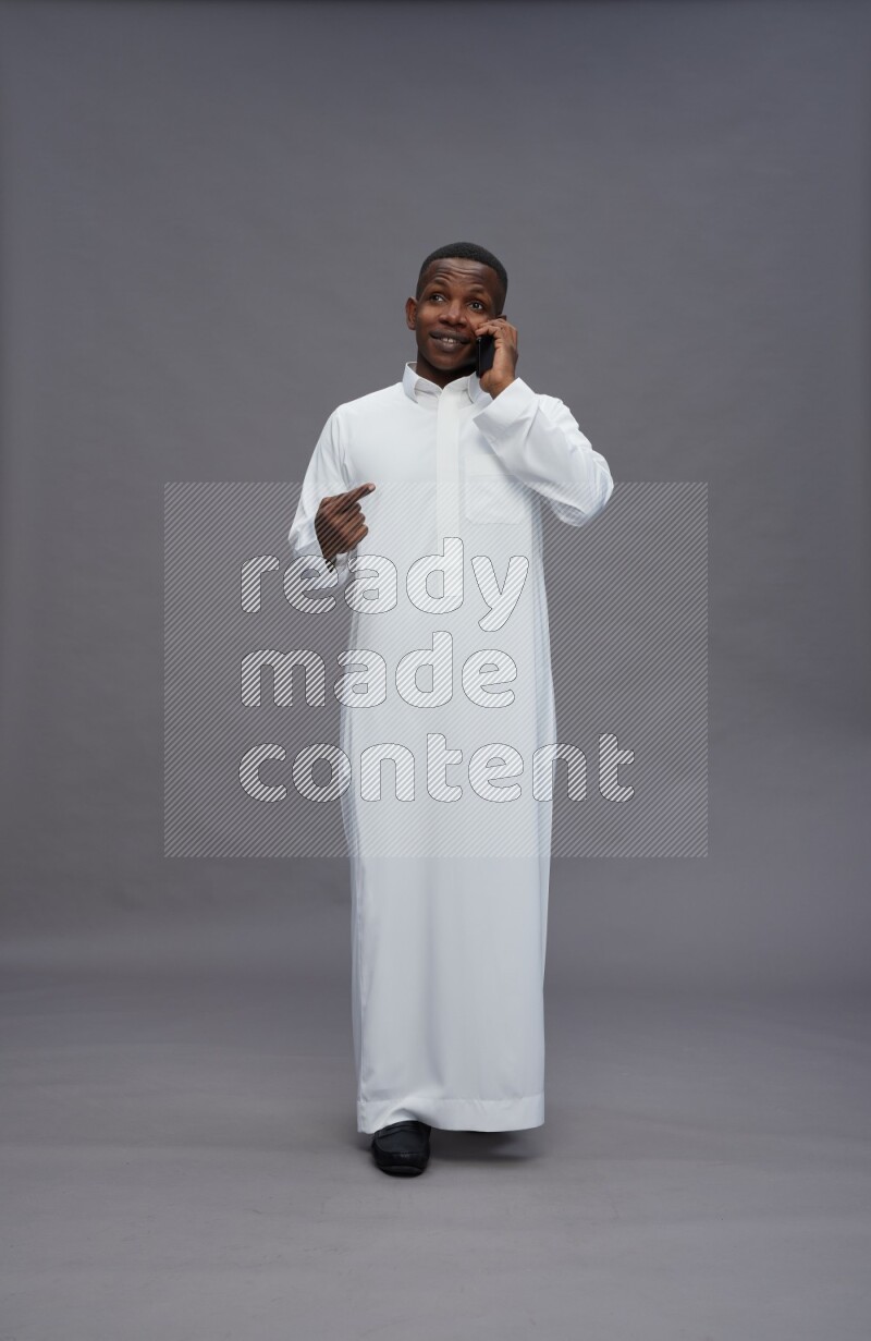 Saudi man wearing thob standing talking on phone on gray background