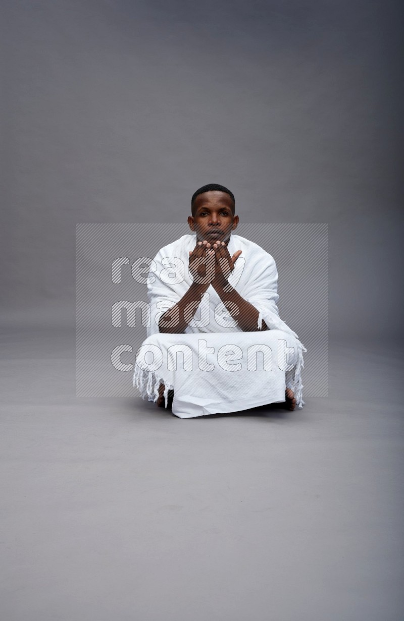 A man wearing Ehram sitting on floor dua'a on gray background