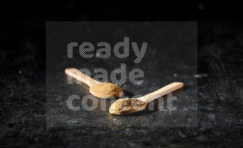 Wooden spoons full of allspice powder on a textured black flooring