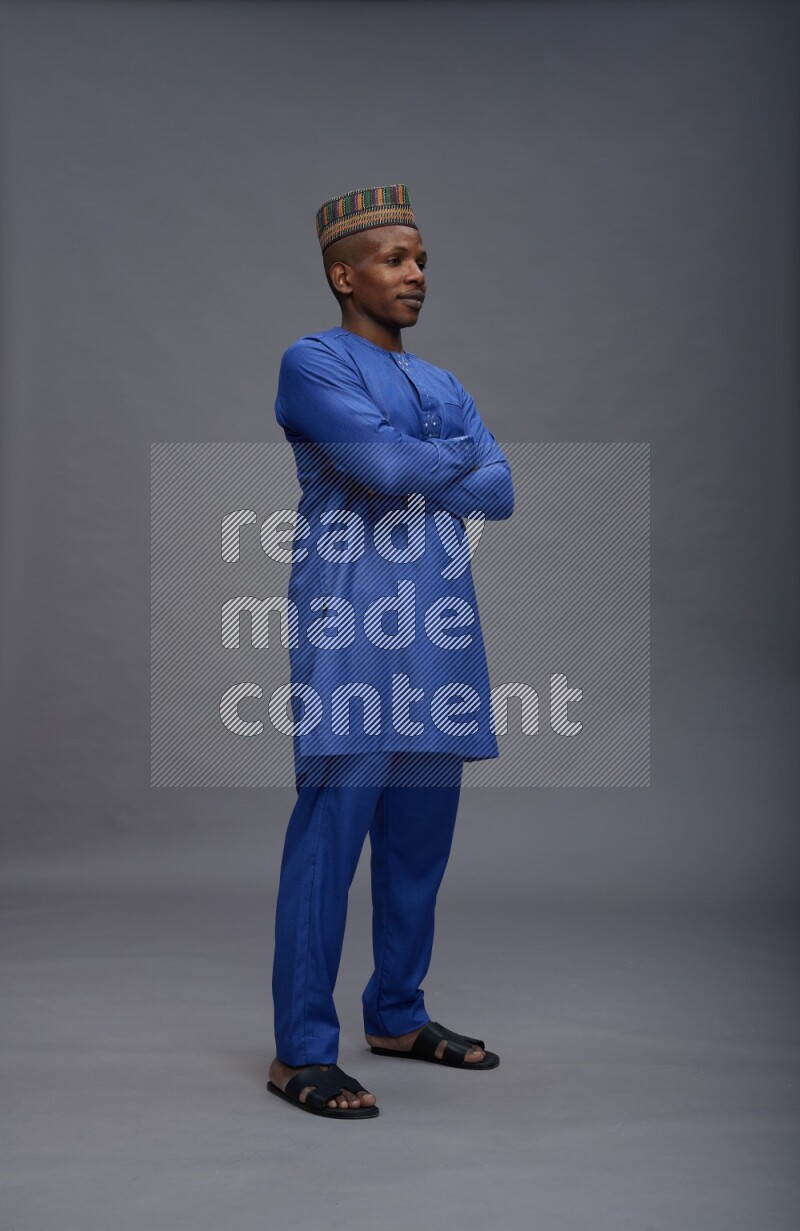 Man wearing Nigerian outfit standing with crossed arms on gray background