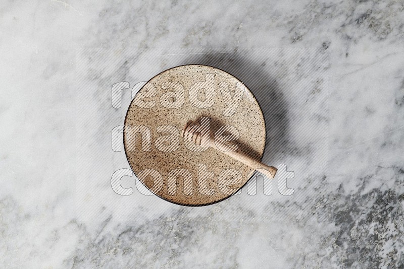 Multicolored Pottery Plate with wooden honey handle in it, on grey marble flooring, Top View