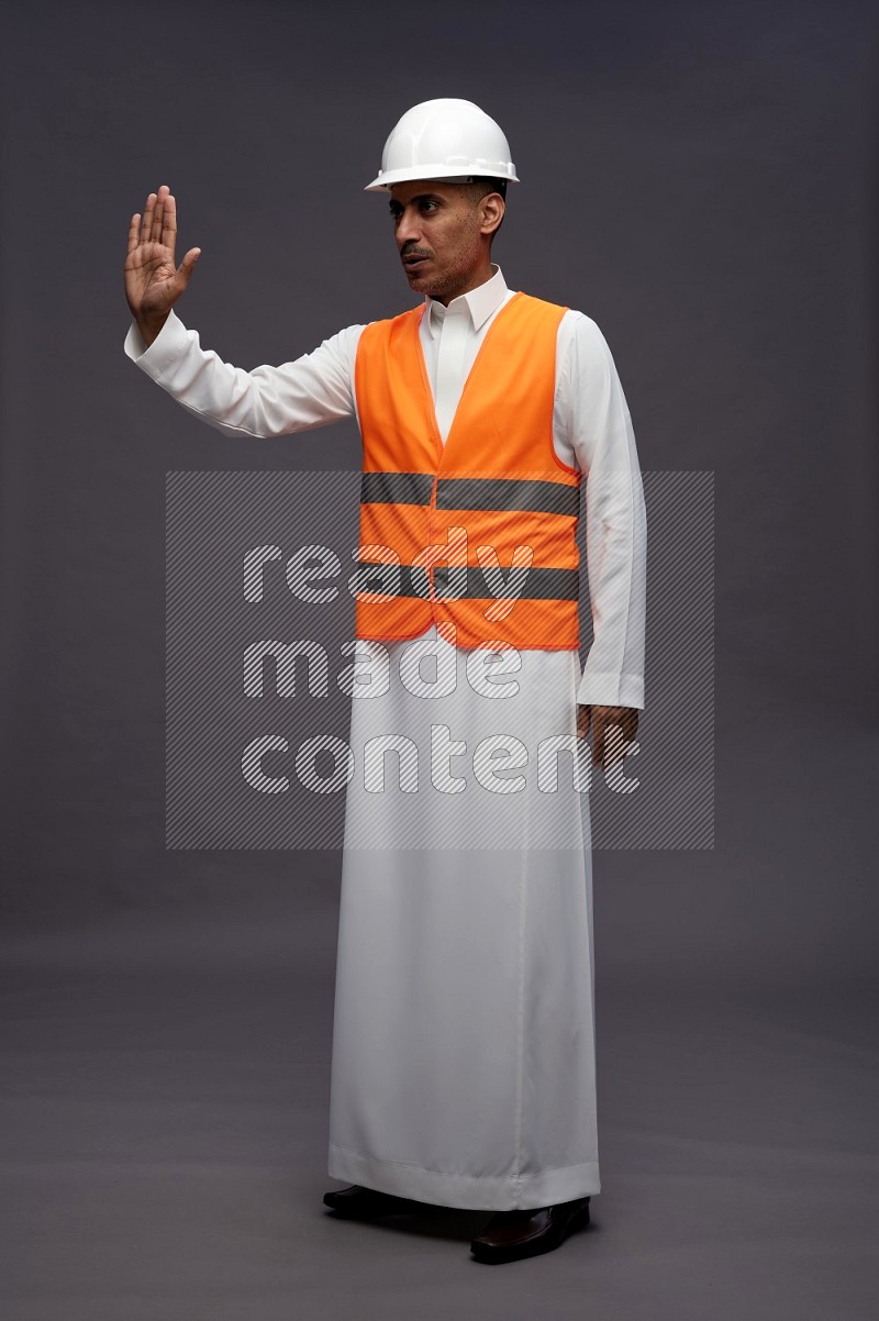 Saudi man wearing thob with engineer vest standing interacting with the camera on gray background