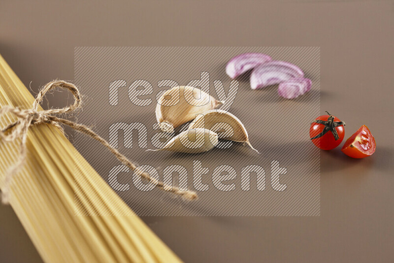 Raw pasta with different ingredients such as cherry tomatoes, garlic, onions, red chilis, black pepper, white pepper, bay laurel leaves, rosemary and cardamom on beige background