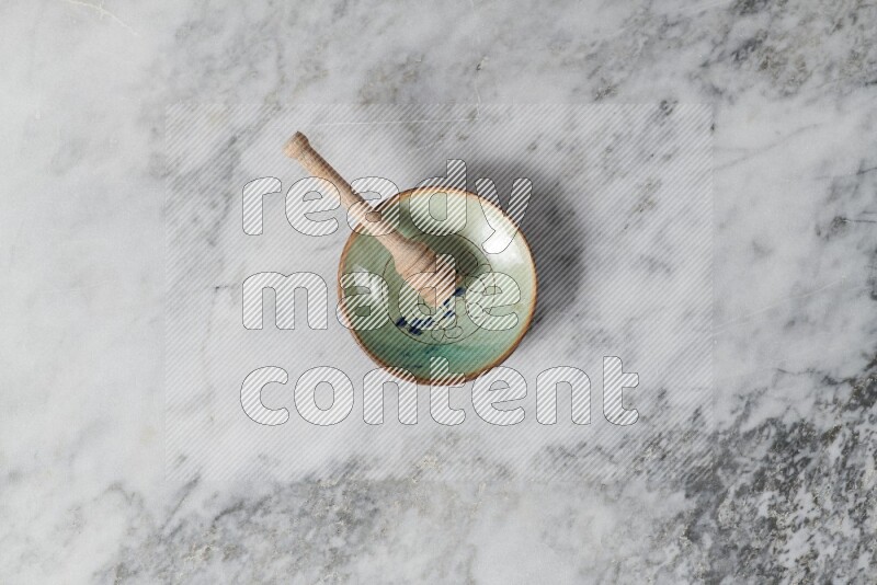 Decorative pottery plate with wooden honey dipper in it on grey marble background