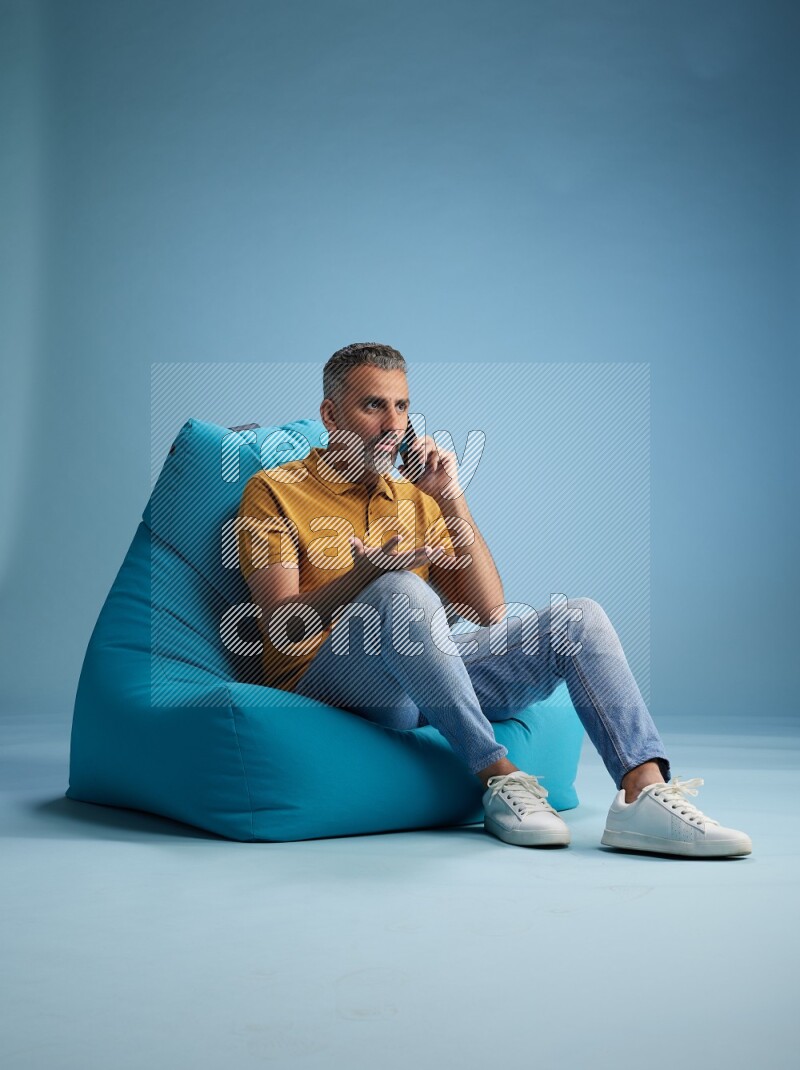 A man sitting on a blue beanbag and talking on the phone