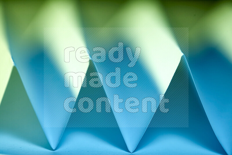 A close-up abstract image showing sharp geometric paper folds in green and blue gradients