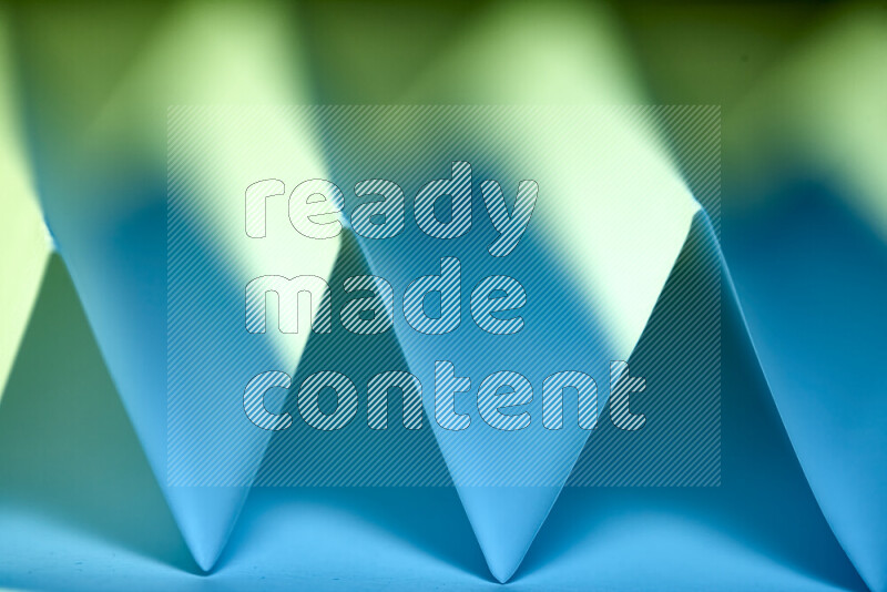 A close-up abstract image showing sharp geometric paper folds in green and blue gradients