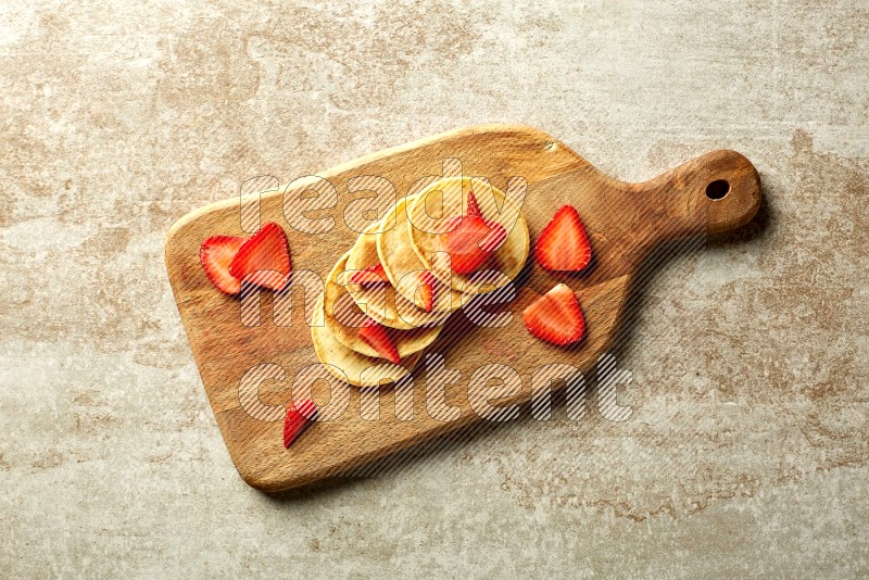 Five stacked strawberry mini pancakes on a wooden board on beige background