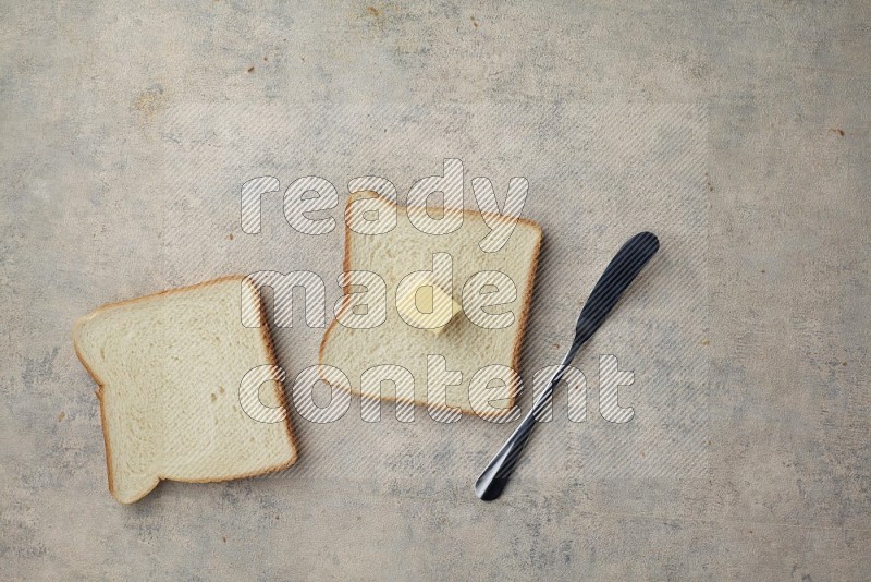 White toast slices with a butter cube and a spreading knife on a light blue textured background