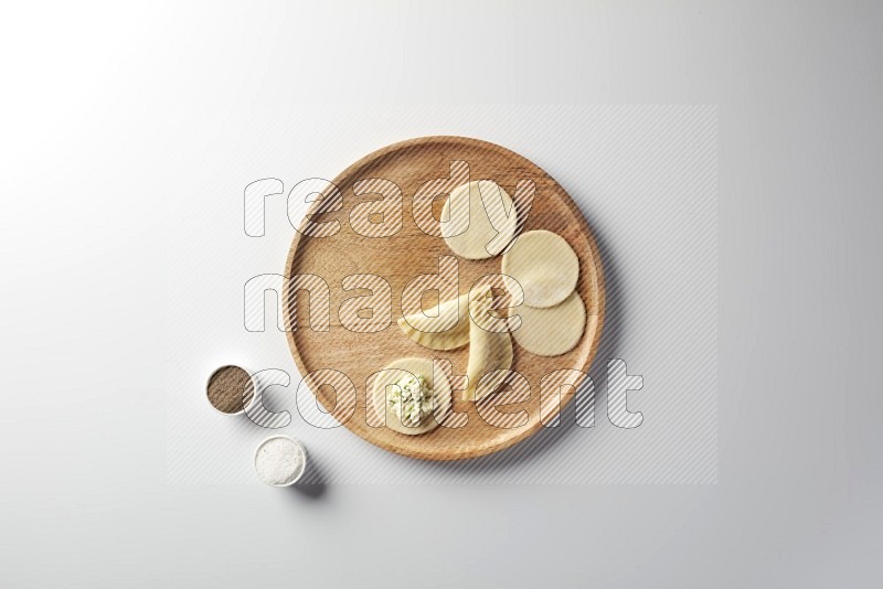 two closed sambosas and one open sambosa filled with cheese while salt, and black pepper aside in a wooden dish on a white background