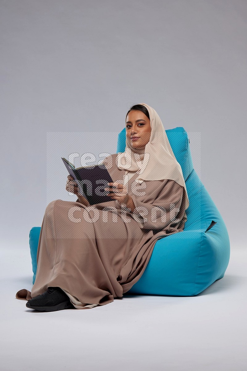 A woman sitting on a blue beanbag and reading a book