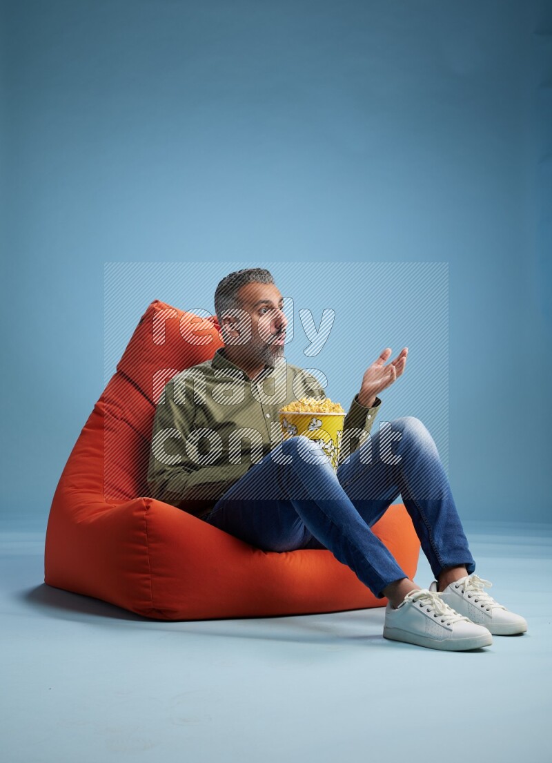 A man sitting on an orange beanbag and eating popcorn