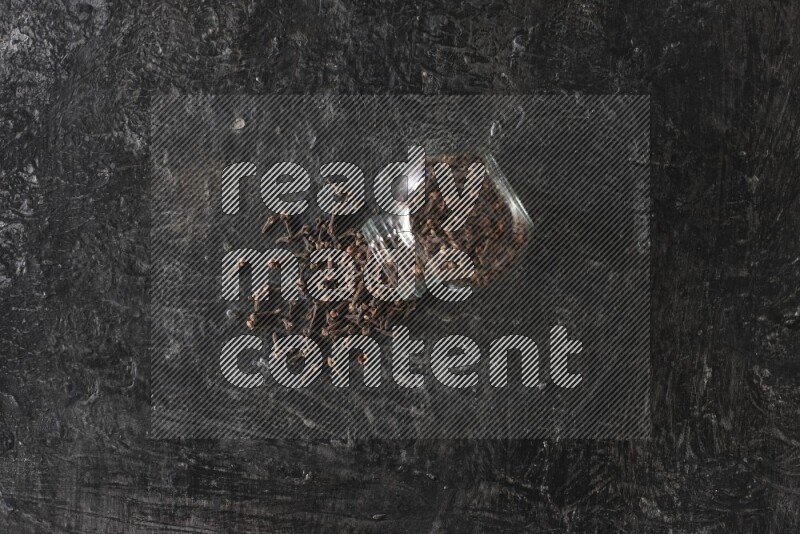 وعاء زجاجي للبهارات مقلوب ممتلئ بالقرنفل والقرنفل سقط منه على أرضية سوداء