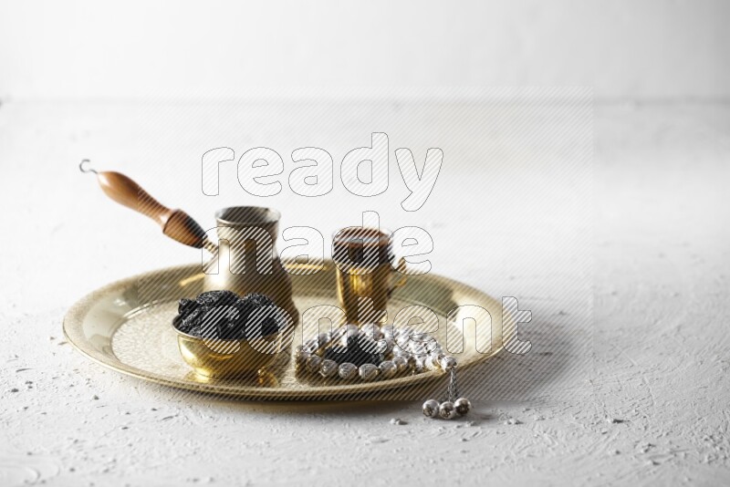 Dried plums in a metal bowl with coffee and prayer beads on a tray in a light setup