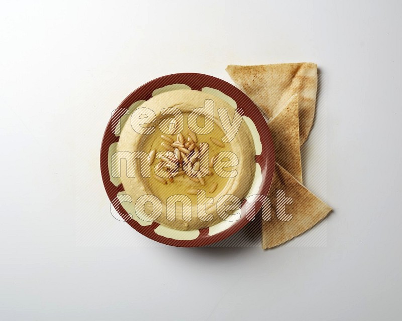 Hummus in a traditional plate garnished with pine nuts on a white background