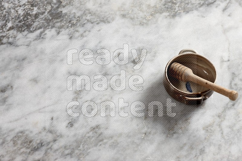 Multicolored Pottery bowl with wooden honey handle in it, on grey marble flooring, 65 degree angle