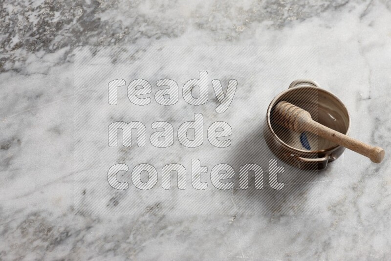 Multicolored pottery bowl with wooden honey dipper in it on grey marble background