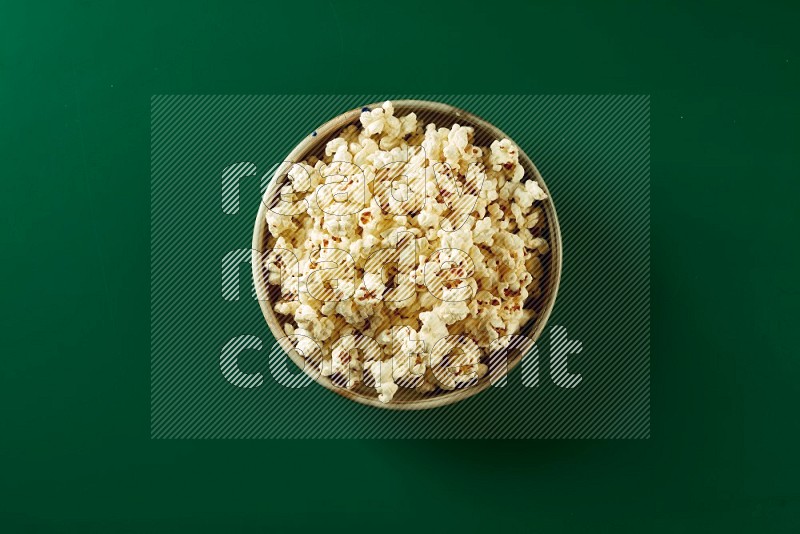 A beige ceramic bowl full of popcorn on a green background in a top view shot
