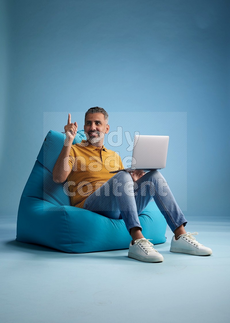 A man sitting on a blue beanbag and working on laptop