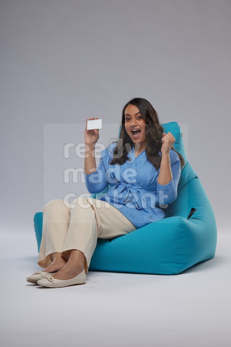 A woman sitting on a blue beanbag and holding ATM card