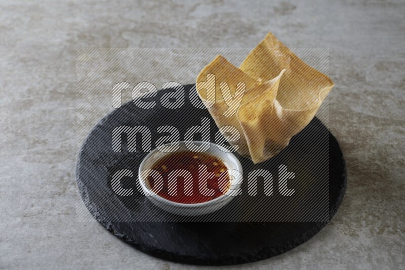 wonton cups with soy sauce ramkin on circle slate on grey textured counter top