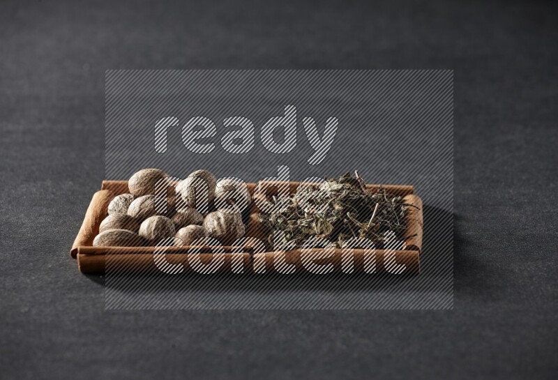 مربعان من أعواد القرفة ممتلئان بجوزة الطيب والريحان المجفف علي خلفية سوداء