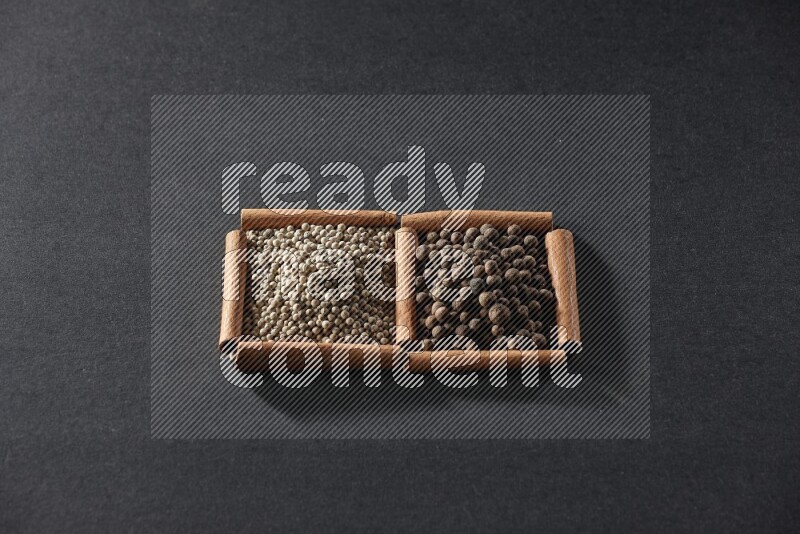 مربعان من أعواد القرفة ممتلئان بحبوب الفلفل الأبيض وحبوب الفلفل الحلو علي خلفية سوداء