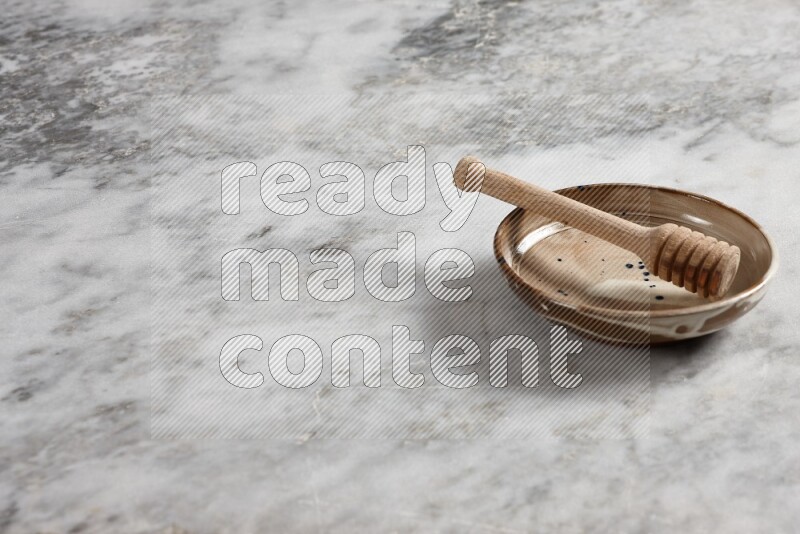 Multicolored pottery plate with wooden honey dipper in it on grey marble background
