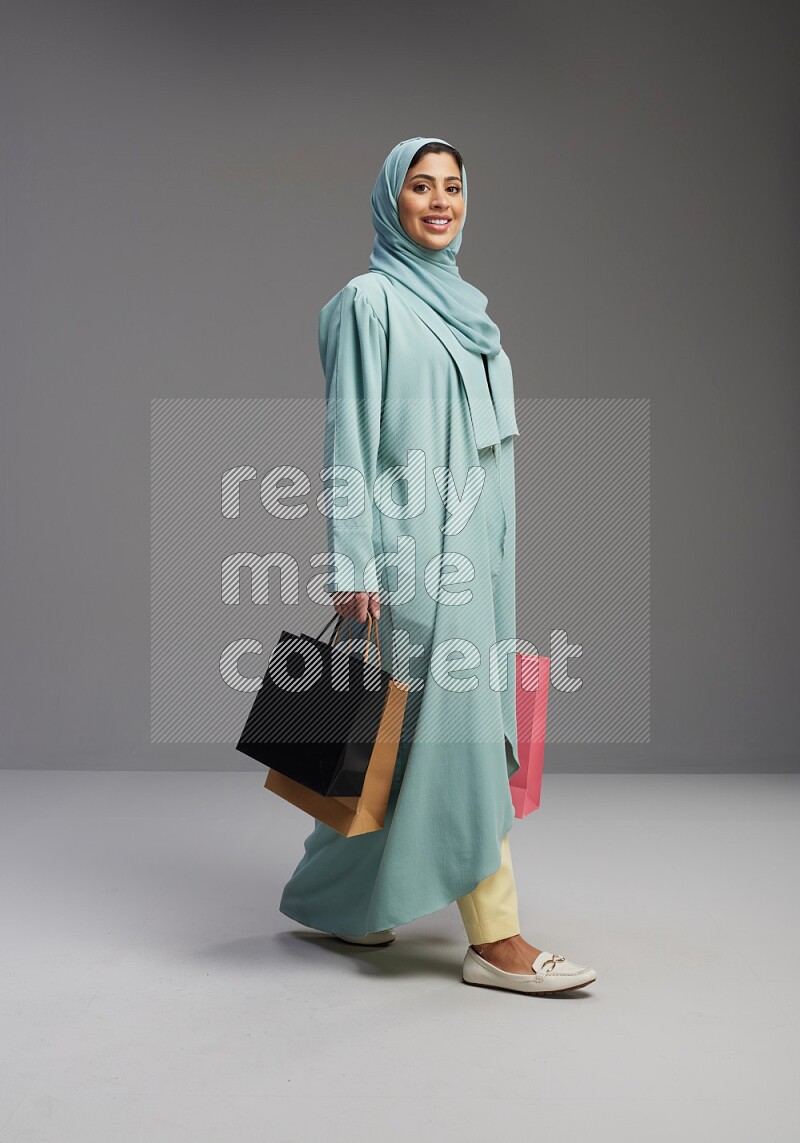 Saudi Woman wearing Abaya standing holding shopping bag on Gray background