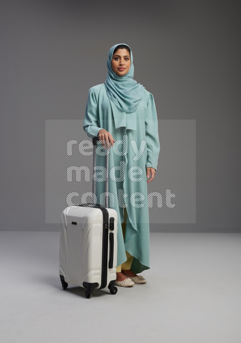 Saudi Woman wearing Abaya standing holding Travel bag on Gray background