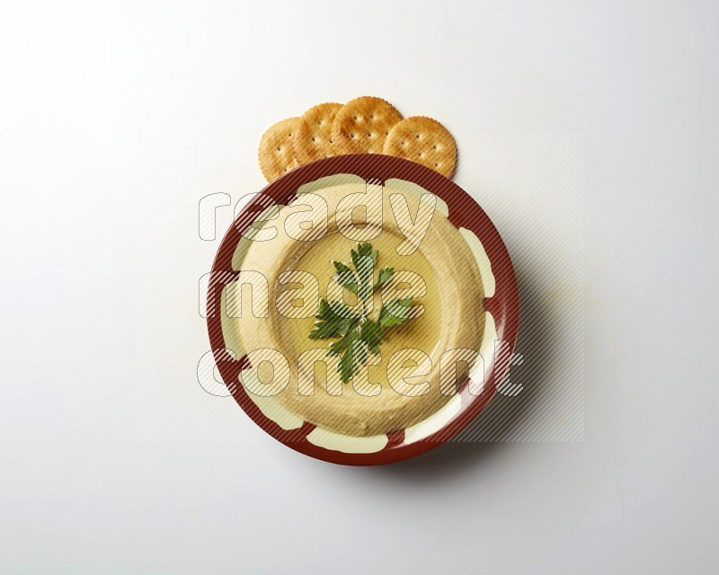 Hummus in a traditional plate garnished with parsley on a white background