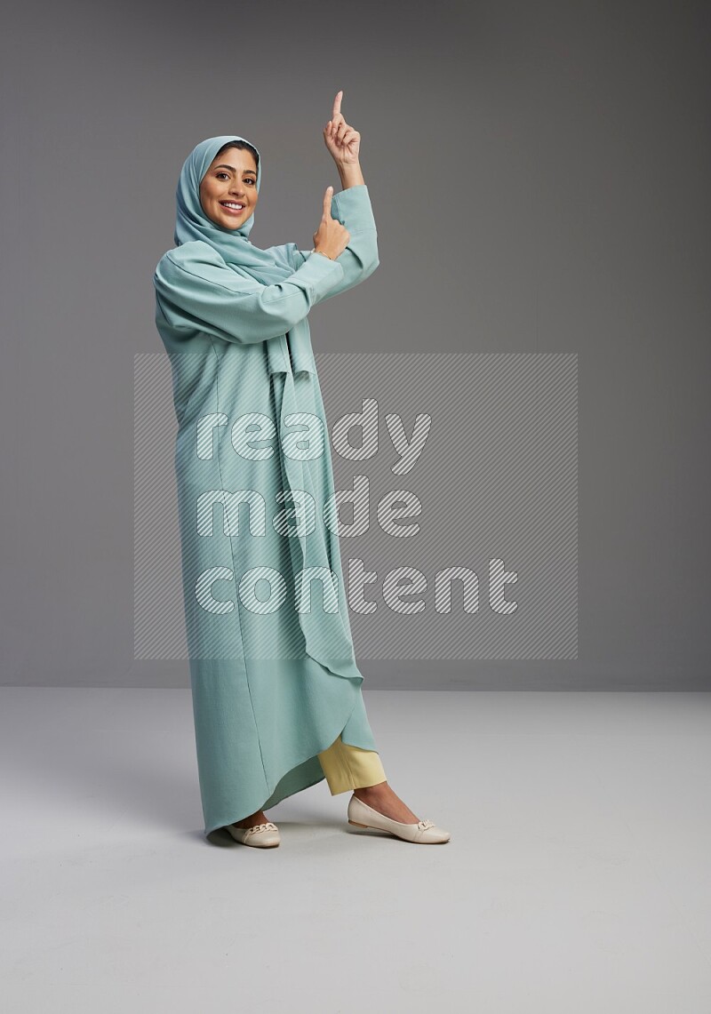 Saudi Woman wearing Abaya standing interacting with the camera on Gray background