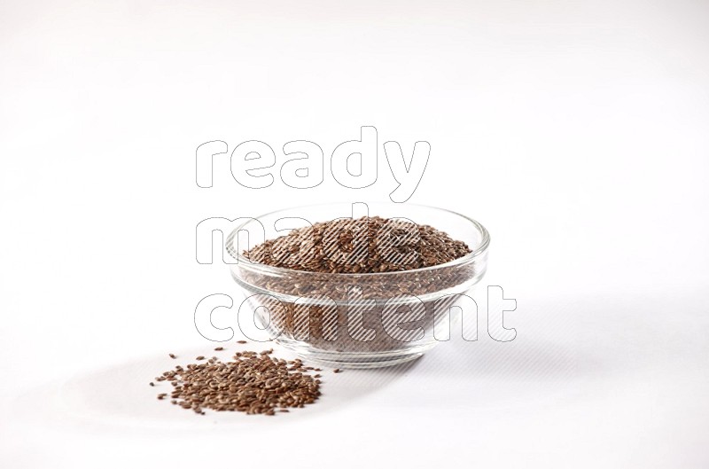 وعاء زجاجي ممتلئ بحبوب بذر الكتان ومحاط بالبذور علي خلفية بيضاء