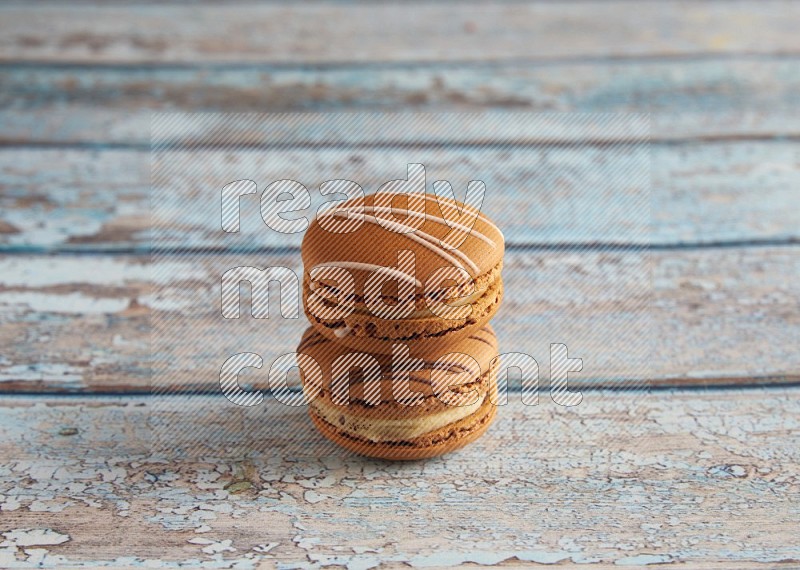 45º Shot of of two assorted Brown Irish Cream, and light brown Almond Cream macarons next to each other on light blue background