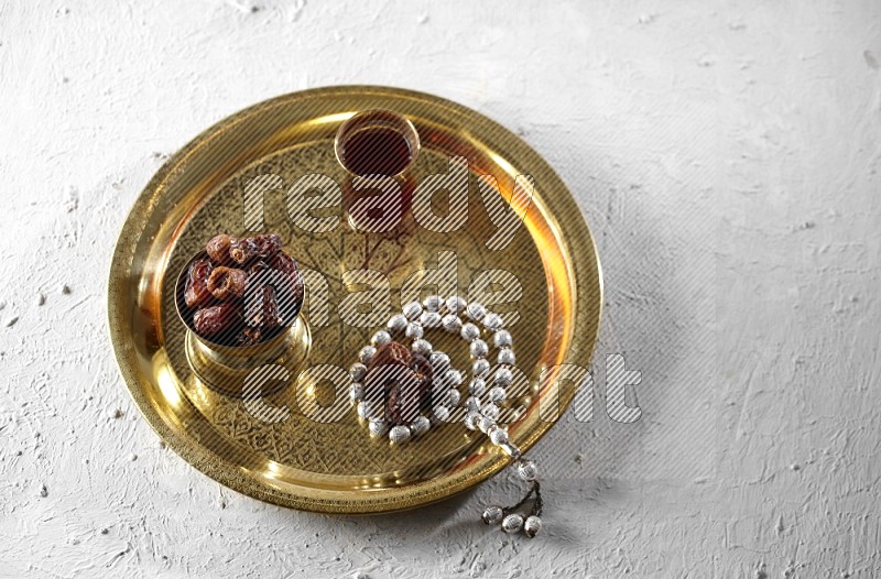 Dates in a metal bowl with tea and prayer beads on a tray in a light setup