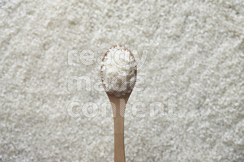 A wooden spoon full of white rice on white rice background