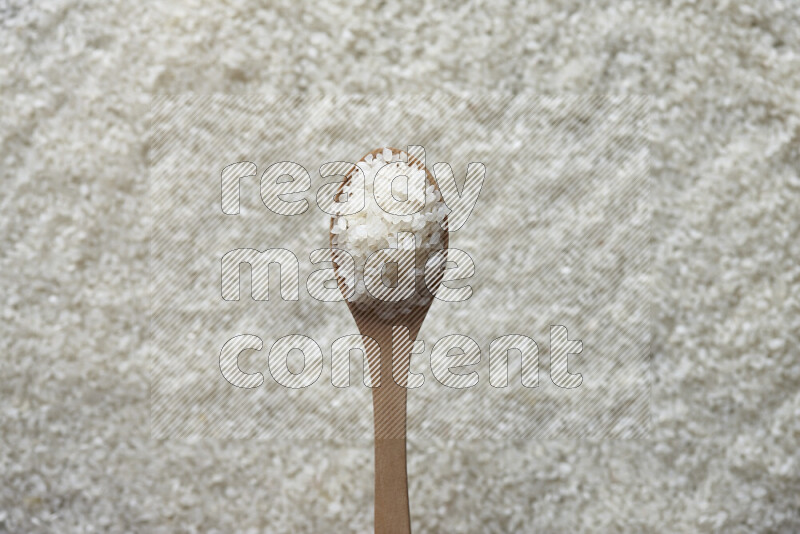 A wooden spoon full of white rice on white rice background