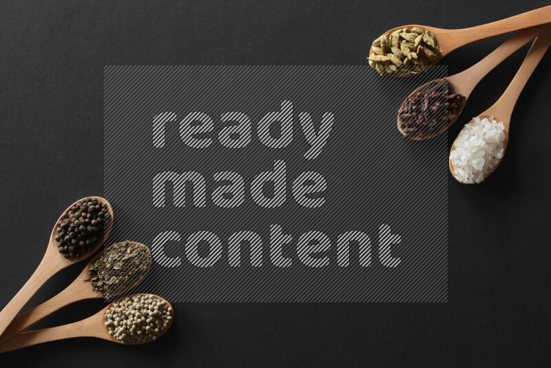 الفلفل الأبيض والقرنفل والهيل والملح والفلفل الأسود وريحان مجفف في معالق خشبية علي خلفية سوداء