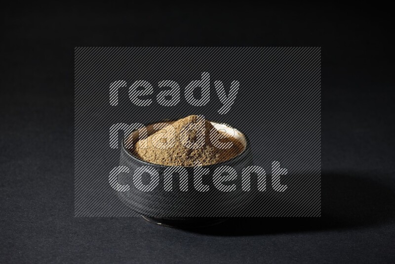 وعاء فخاري أسود ممتلئ ببودرة الكمون على خلفية سوداء