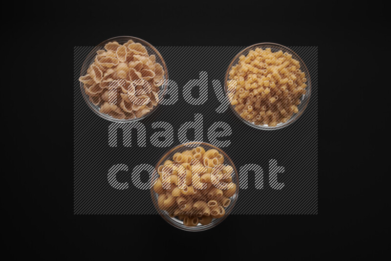 Different pasta types in glass bowls on black background