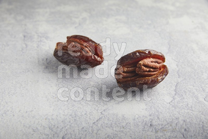 two pecan stuffed madjoul dates on a light grey background