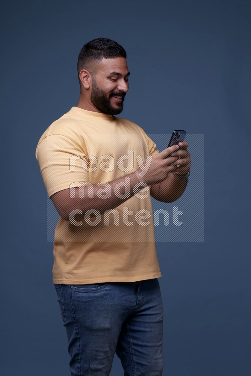 A man Texting on his phone on Blue Background wearing Orange T-shirt