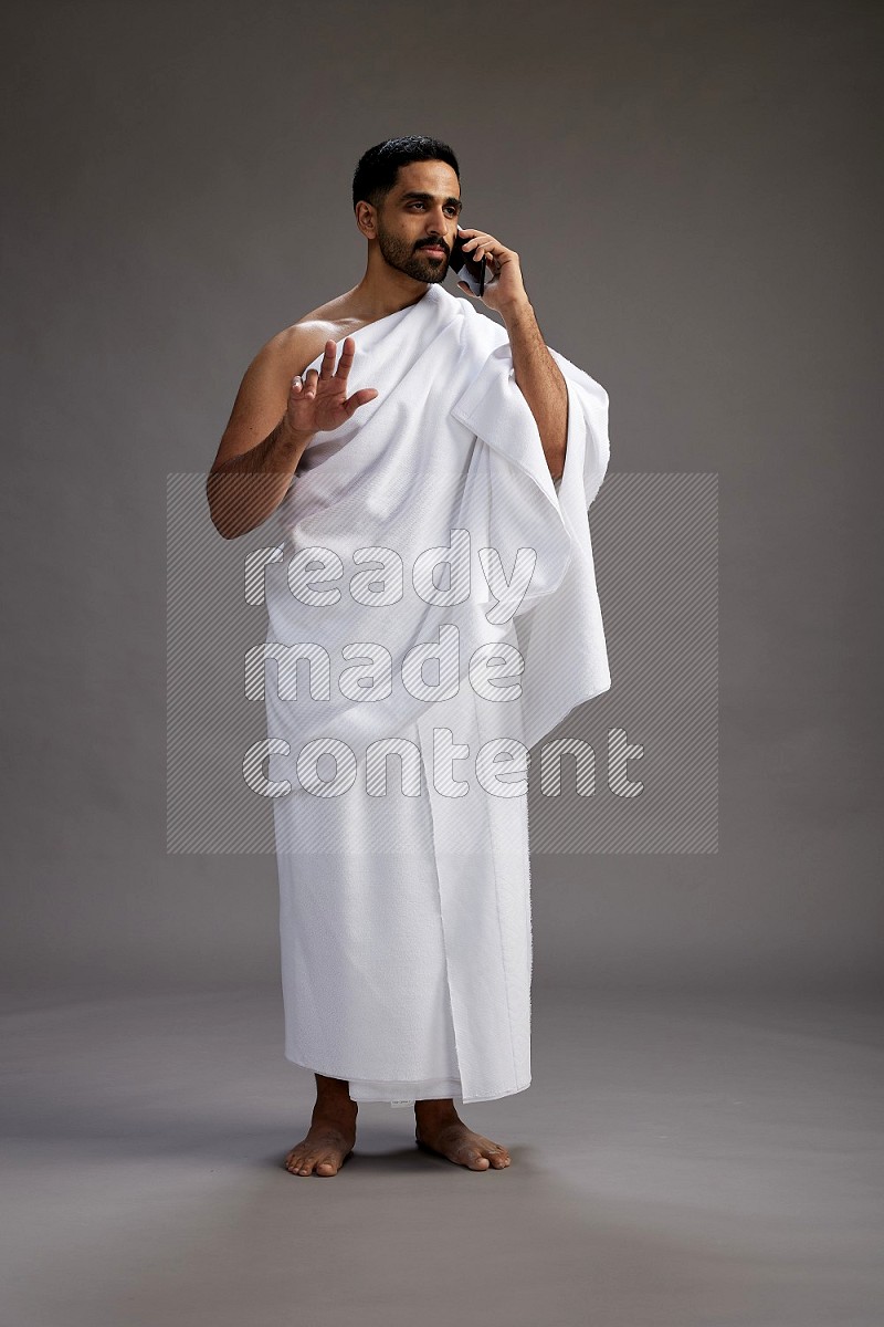 A man wearing Ehram Standing talking on phone on gray background