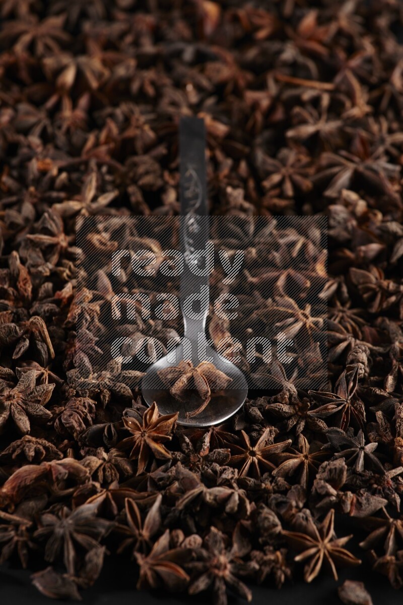 اليانسون النجمي في ملعقة معدنية فوق اليانسون النجمي الذي يغطي الإطار على أرضية سوداء