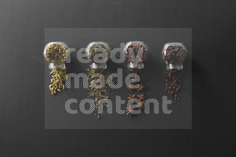 4 glass spice jars full of cloves, cardamom, basil and star anise on black flooring