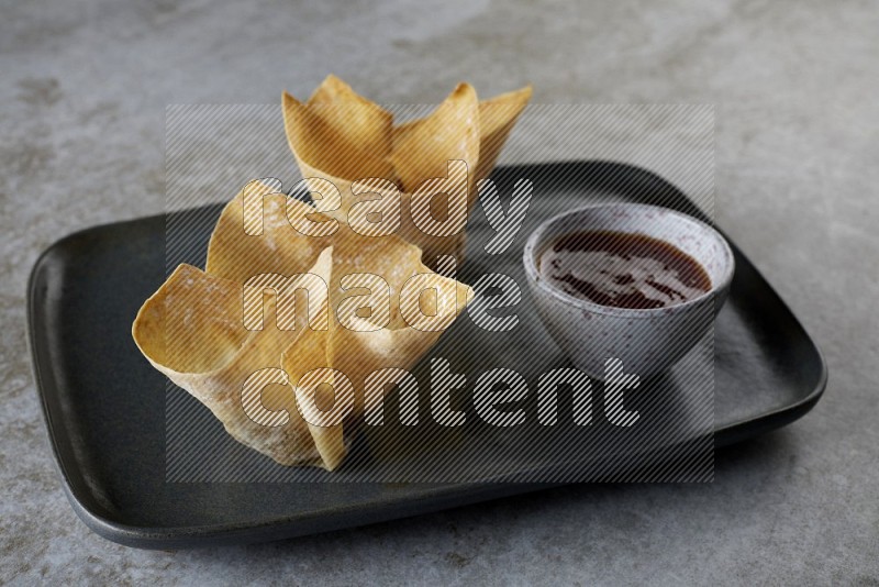 wonton cups with soy sauce ramkin on rectangle dark grey ceramic plate on grey textured counter top