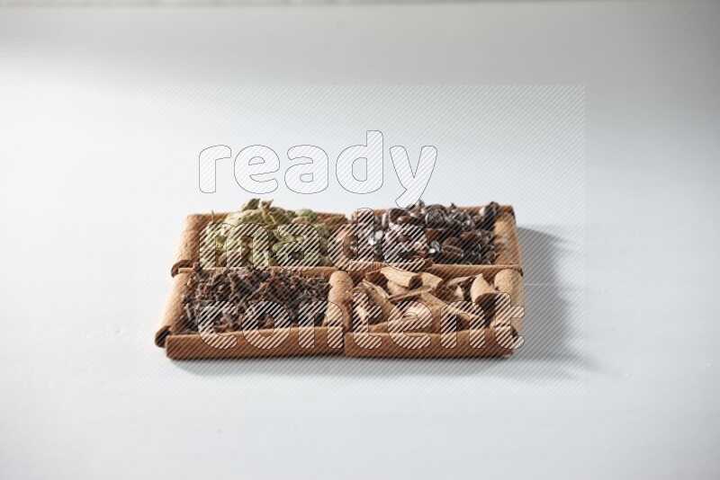 4 مربعات من أعواد القرفة ممتلئة بحبوب القهوة والقرفة والقرنفل والهيل على أرضية بيضاء