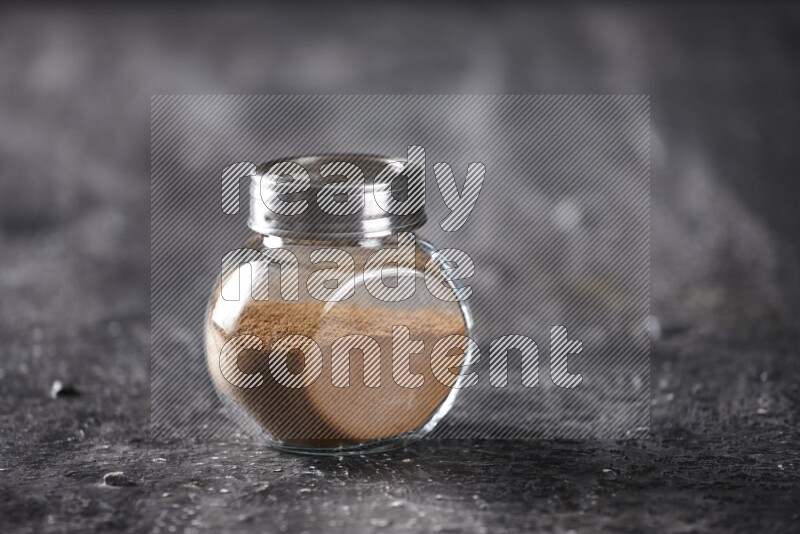 Herbal glass jar full of cinnamon powder on a textured black background
