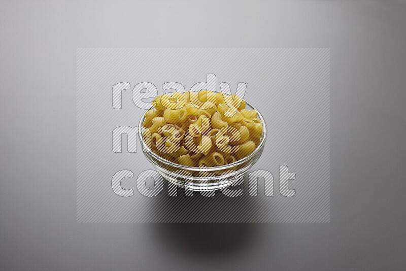 Elbow pasta in a glass bowl on grey background